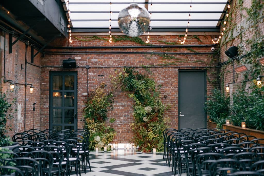 A brick-walled ceremony space set with chairs and a floral arch